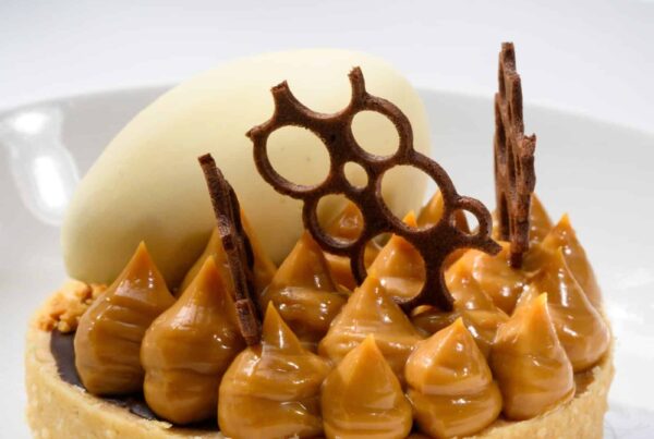 Creamy caramel tart with chocolate decorations, topped with white chocolate curl, served on a white plate at Palm House Boutique Hotel and Spa.