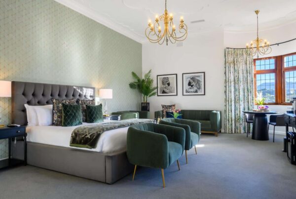 Luxurious hotel bedroom with a plush bed, elegant green armchairs, and stylish decor at Palm House Boutique Hotel and Spa, offering a relaxing and sophisticated stay in South Africa.